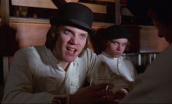 Movie still from “A Clockwork Orange” (1971), directed by Stanley Kubrick – A man wearing a black hat is holding a glass of beer; Close Up shot, Low angle