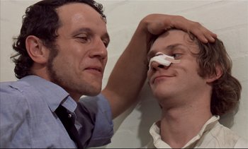 Movie still from “A Clockwork Orange” (1971), directed by Stanley Kubrick – A man putting a bandage on another man's face; Close Up shot, Low angle