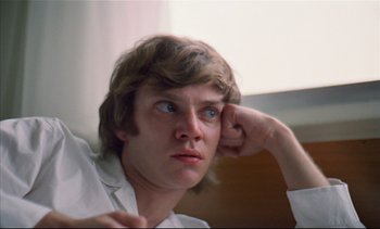 Movie still from “A Clockwork Orange” (1971), directed by Stanley Kubrick – A young man with long brown hair and blue eyes looks at the camera; Close Up shot, Low angle