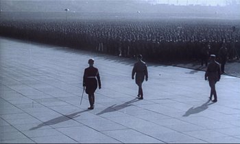 Two people walking on a sidewalk near a crowd of people