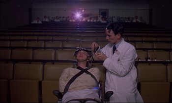 Movie still from “A Clockwork Orange” (1971), directed by Stanley Kubrick – A man sitting in front of a man in a chair; Wide shot, Low angle