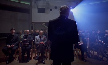 Movie still from “A Clockwork Orange” (1971), directed by Stanley Kubrick – A group of people sitting in a room with a man standing in front of them; Wide shot, Low angle