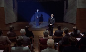 Movie still from “A Clockwork Orange” (1971), directed by Stanley Kubrick – A group of people sitting in front of a stage; Wide shot, High angle