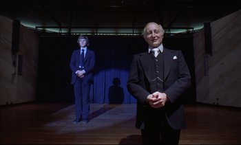 Movie still from “A Clockwork Orange” (1971), directed by Stanley Kubrick – A man in a suit and tie standing next to another man in a suit and tie; Medium shot, Low angle