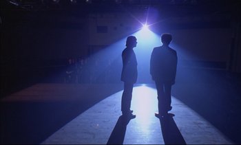 Movie still from “A Clockwork Orange” (1971), directed by Stanley Kubrick – Two men standing on a runway in front of a spotlight; Wide shot, Low angle