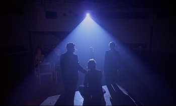 Movie still from “A Clockwork Orange” (1971), directed by Stanley Kubrick – A group of people standing on a stage under a spotlight; Wide shot, High angle