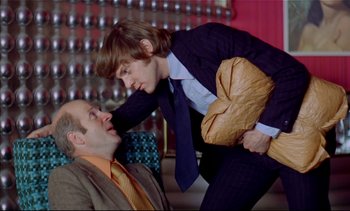 Movie still from “A Clockwork Orange” (1971), directed by Stanley Kubrick – A man and a woman in business attire face each other; Medium shot, Low angle