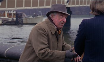 Movie still from “A Clockwork Orange” (1971), directed by Stanley Kubrick – An older man wearing a brown hat and coat; Medium shot, Over the shoulder angle