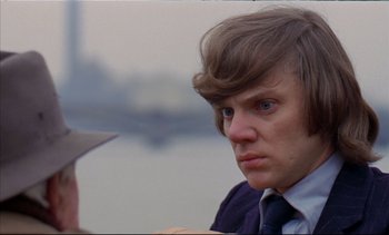 Movie still from “A Clockwork Orange” (1971), directed by Stanley Kubrick – A young man with long brown hair wearing a suit and tie; Close Up shot, Over the shoulder angle