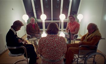 Movie still from “A Clockwork Orange” (1971), directed by Stanley Kubrick – A group of people sitting around a glass table in a room; Wide shot, High angle