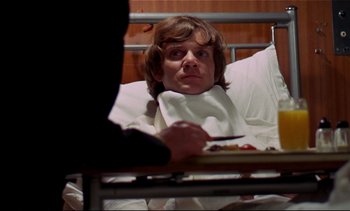 Movie still from “A Clockwork Orange” (1971), directed by Stanley Kubrick – A man sitting in a hospital bed looking at the camera; Medium shot, Low angle