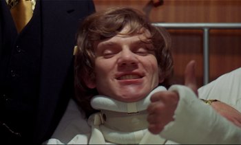 Movie still from “A Clockwork Orange” (1971), directed by Stanley Kubrick – A man wearing a neck brace is sitting in a chair; Close Up shot, Low angle
