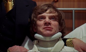 Movie still from “A Clockwork Orange” (1971), directed by Stanley Kubrick – A man wearing a neck brace while standing next to another man; Close Up shot, Low angle