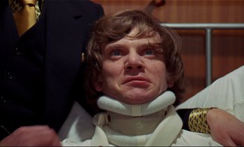 Movie still from “A Clockwork Orange” (1971), directed by Stanley Kubrick – A man wearing a neck brace while standing next to another man; Close Up shot, Low angle