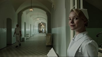 Movie still from “A Cure for Wellness” (2016), directed by Gore Verbinski – A woman standing in a hallway holding a book; Medium shot, Low angle