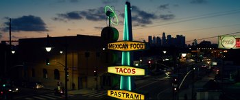 Movie still from “Ambulance” (2022), directed by Michael Bay – A neon sign that reads " mexican food tacos pastrami "; Extreme Wide shot, Low angle