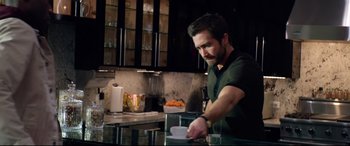 Movie still from “Ambulance” (2022), directed by Michael Bay – A man in a green shirt is in a kitchen; Medium shot, Over the shoulder angle