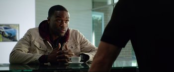 Movie still from “Ambulance” (2022), directed by Michael Bay – A man sitting at a table with a cup of coffee in front of him; Close Up shot, Over the shoulder angle