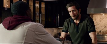 Movie still from “Ambulance” (2022), directed by Michael Bay – A man sitting in front of another man in front of a counter; Medium shot, Over the shoulder angle