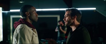 Movie still from “Ambulance” (2022), directed by Michael Bay – Two men standing next to each other in a dark room; Medium shot, Over the shoulder angle
