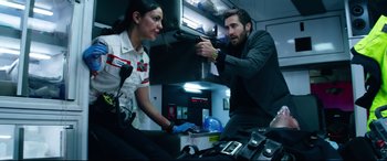 Movie still from “Ambulance” (2022), directed by Michael Bay – A man pointing a gun at a woman in a room; Medium shot, Low angle