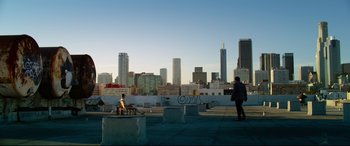Movie still from “Ambulance” (2022), directed by Michael Bay – A person standing on top of a building near some buildings; Extreme Wide shot, Low angle