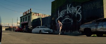 Movie still from “Ambulance” (2022), directed by Michael Bay – A man standing in front of a car on the side of the road; Wide shot, Low angle