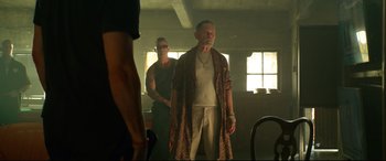 Movie still from “Ambulance” (2022), directed by Michael Bay – A man standing in front of another man in a room; Medium shot, Low angle