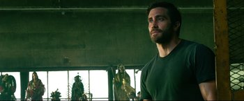 Movie still from “Ambulance” (2022), directed by Michael Bay – A man standing in front of a statue in a room; Medium shot, Over the shoulder angle