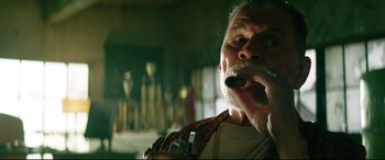 Movie still from “Ambulance” (2022), directed by Michael Bay – An older man smoking a cigarette in a dark room; Close Up shot, Low angle