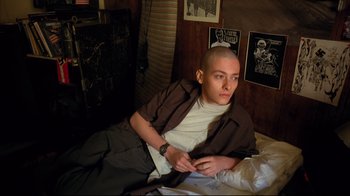 Movie still from “American History X” (1998), directed by Tony Kaye – A man sitting on a bed with a shaved head; Medium shot, High angle
