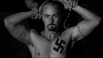 Movie still from “American History X” (1998), directed by Tony Kaye – A man with a tattoo on his chest holding handcuffed hands; Close Up shot, High angle