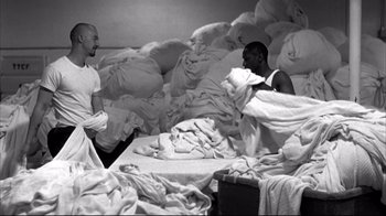 Movie still from “American History X” (1998), directed by Tony Kaye – Two men are sitting on a bed in a room full of unmade sheets; Wide shot, High angle