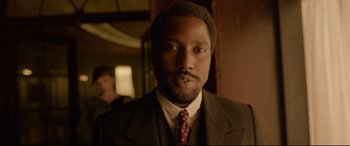 Movie still from “Amsterdam” (2022), directed by David O. Russell – A man in a suit and tie in a room; Close Up shot, Low angle