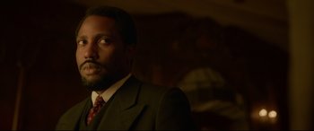 Movie still from “Amsterdam” (2022), directed by David O. Russell – A man wearing a suit and tie in a room; Close Up shot, Over the shoulder angle