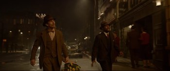 Movie still from “Amsterdam” (2022), directed by David O. Russell – Two men walking down a street holding a basket of fruit; Medium shot, Over the shoulder angle