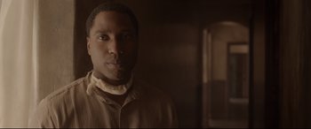 Movie still from “Amsterdam” (2022), directed by David O. Russell – A man in a brown shirt is standing in a room; Close Up shot, Over the shoulder angle