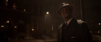 Movie still from “Amsterdam” (2022), directed by David O. Russell – A man wearing a suit and a hat standing in the dark; Medium shot, Over the shoulder angle