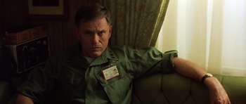 Movie still from “Apocalypse Now” (1979), directed by Francis Ford Coppola – A man sitting on a couch wearing a green shirt; Close Up shot, Low angle