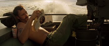 Movie still from “Apocalypse Now” (1979), directed by Francis Ford Coppola – A person sitting on a boat holding a banana; Medium shot, High angle