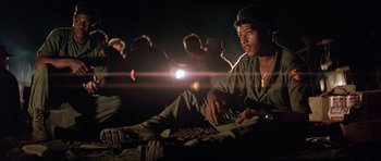 Movie still from “Apocalypse Now” (1979), directed by Francis Ford Coppola – A group of men sitting on the ground in the dark; Medium shot, Low angle