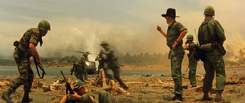 Movie still from “Apocalypse Now” (1979), directed by Francis Ford Coppola – A group of men in green uniforms standing next to a fire pit; Wide shot, Low angle