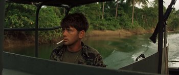 Movie still from “Apocalypse Now” (1979), directed by Francis Ford Coppola – A man sitting in a boat smoking a cigarette; Close Up shot, Over the shoulder angle