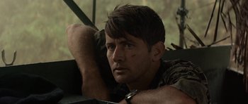 Movie still from “Apocalypse Now” (1979), directed by Francis Ford Coppola – A person sitting on the ground; Close Up shot, Low angle