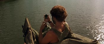 Movie still from “Apocalypse Now” (1979), directed by Francis Ford Coppola – A man sitting in a boat on the water taking a picture; Medium shot, High angle
