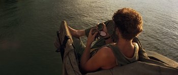 Movie still from “Apocalypse Now” (1979), directed by Francis Ford Coppola – A man sitting on the ground looking at a camera; Medium shot, High angle