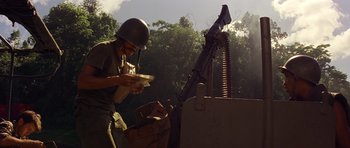 Movie still from “Apocalypse Now” (1979), directed by Francis Ford Coppola – A man holding a cat while standing next to a machine gun; Medium shot, Low angle