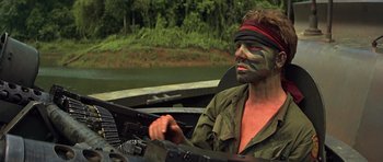Movie still from “Apocalypse Now” (1979), directed by Francis Ford Coppola – A man with a face paint sitting in the back of a boat in the water; Medium shot, Low angle