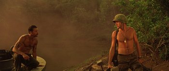 Movie still from “Apocalypse Now” (1979), directed by Francis Ford Coppola – A man in a hat and a shirt standing next to a body of water; Medium shot, Low angle