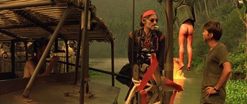 Movie still from “Apocalypse Now” (1979), directed by Francis Ford Coppola – A man sitting on the ground smoking a cigarette; Wide shot, Low angle